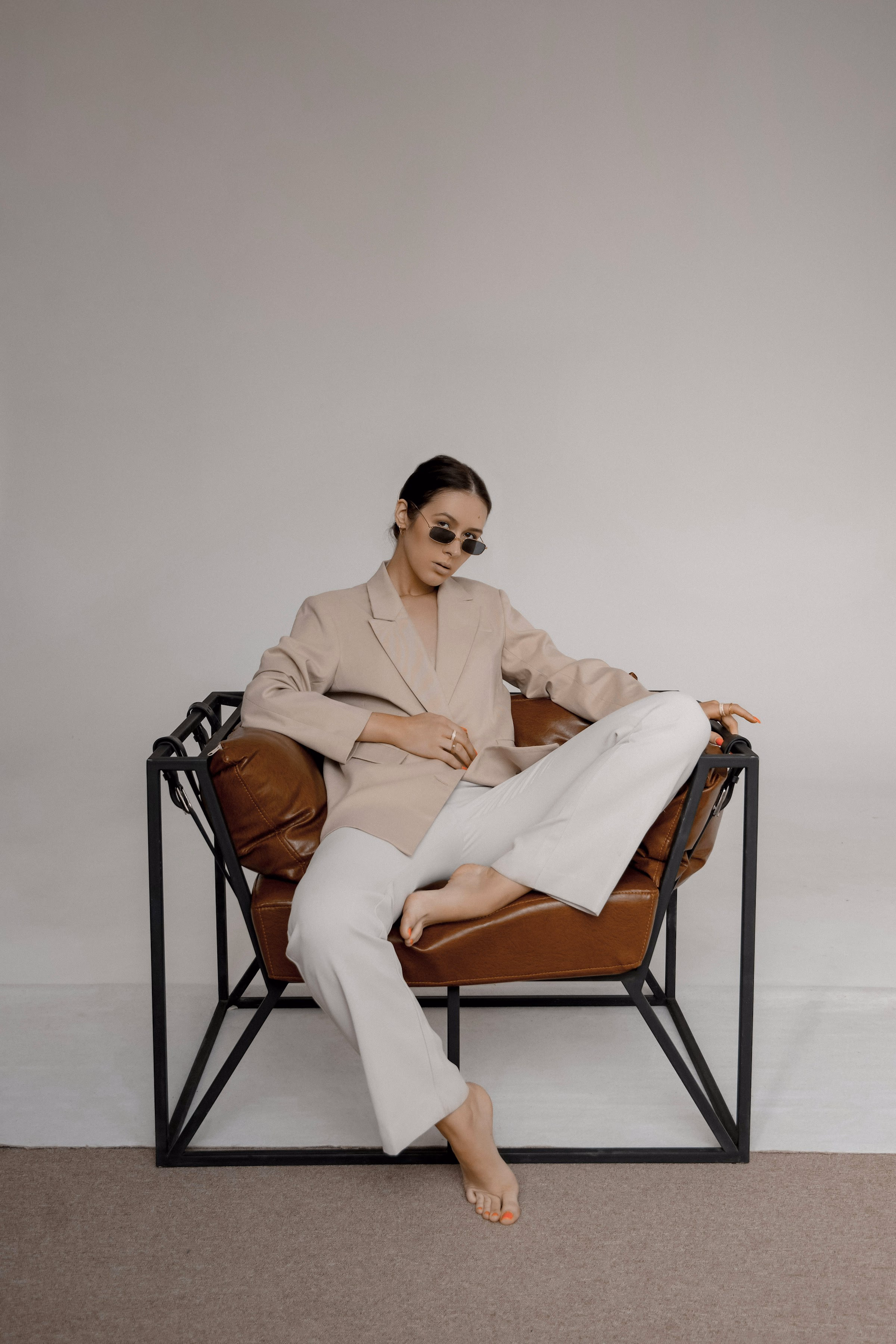 Mulher de terno creme sentada numa poltrona, estúdio claro